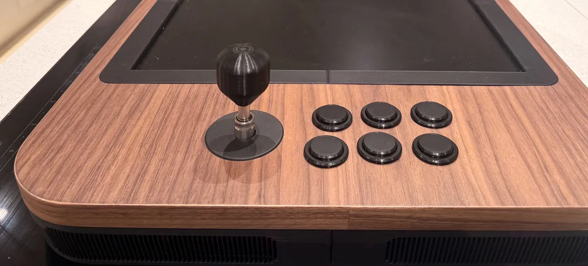 Photo of the real table from one end: walnut top, a black ball-top stick and six black buttons, the screen behind them